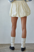 Person wearing a light-colored skirt, white socks, and black shoes against a plain background