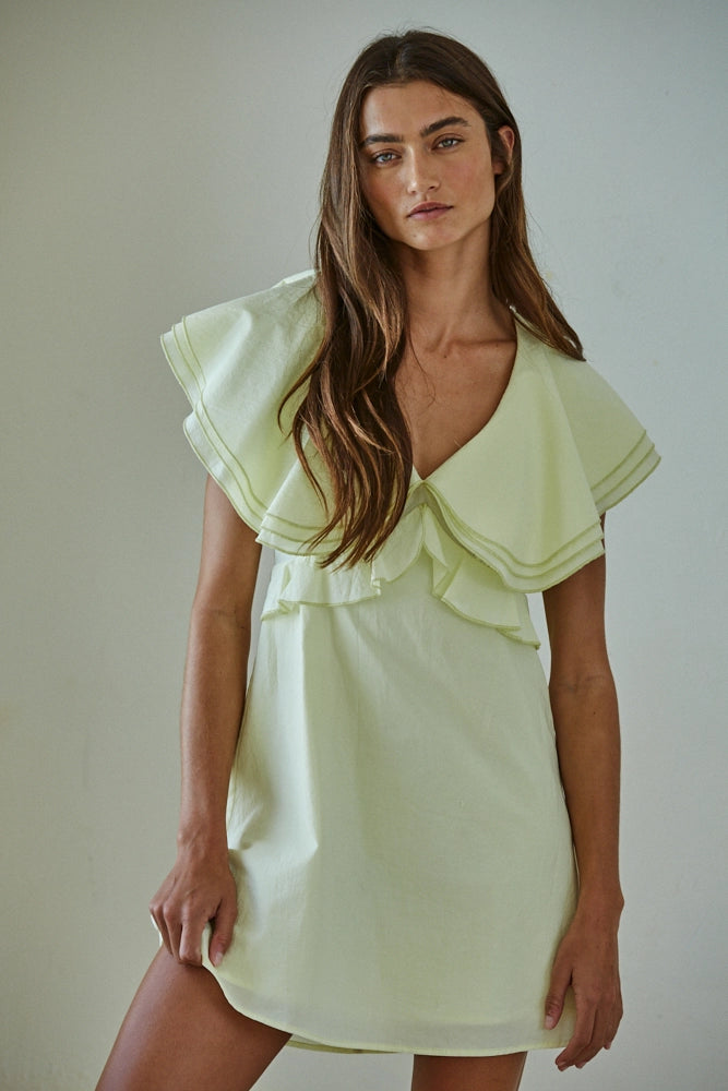 Woman wearing a light green dress with ruffled details against a neutral background