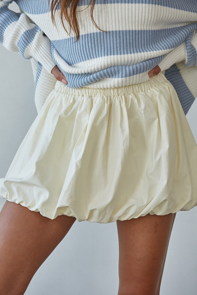 Person wearing a blue and white striped sweater and cream-colored shorts on a plain background