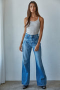 Woman wearing a white tank top and blue jeans against a plain background