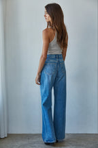 Woman wearing blue jeans and a white top against a plain background